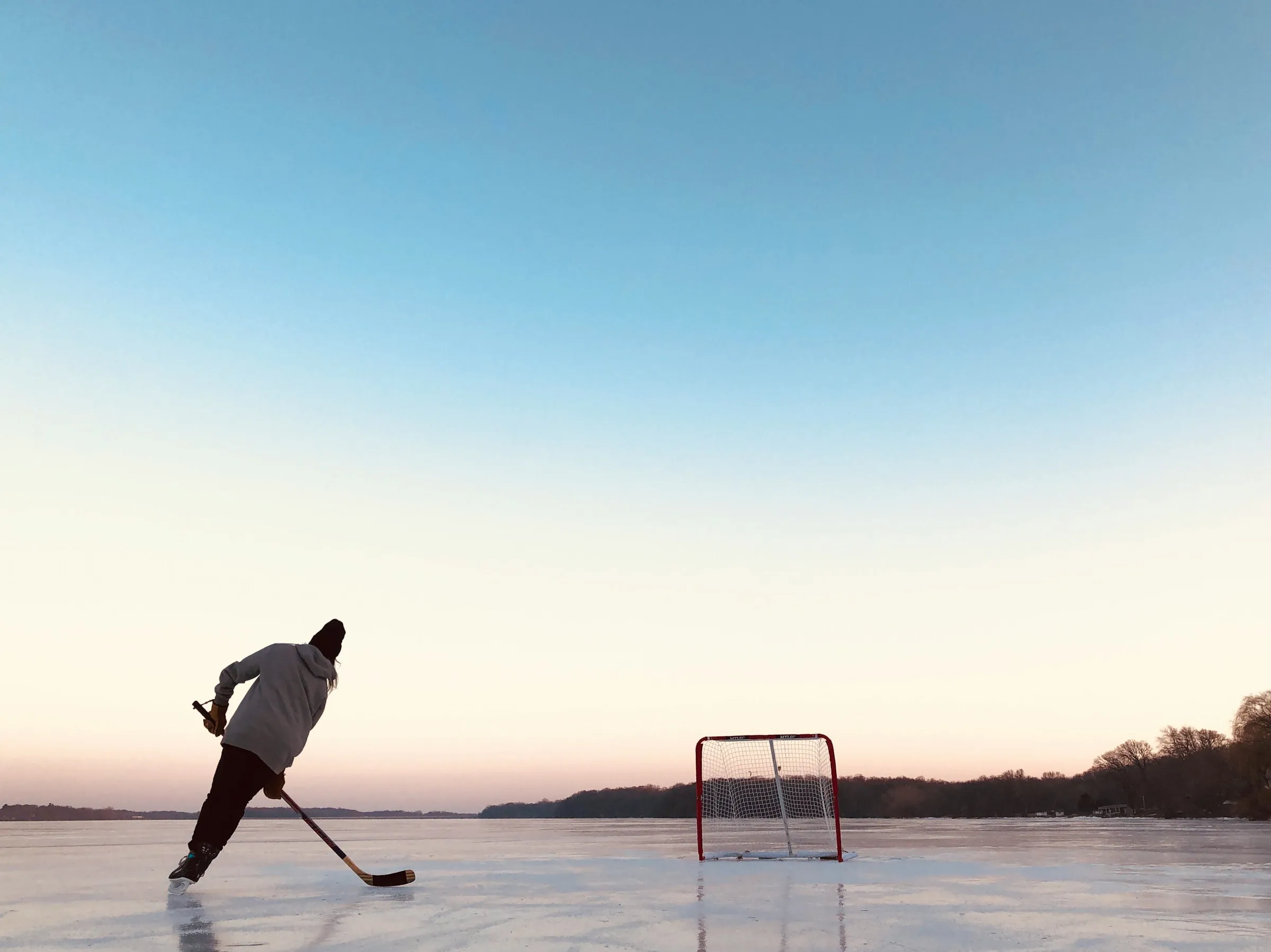 Ein Spieler mit Schläger auf einem zugefrorenen See in der Abenddämmerung