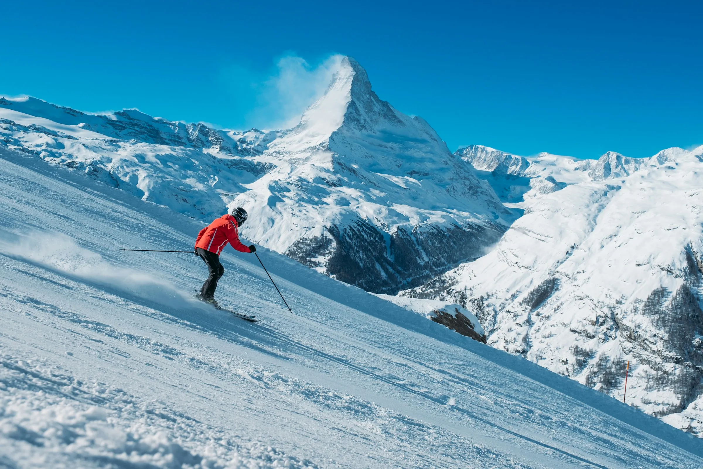Skifahrer in roter Jacke auf einer sonnigen Piste vor Bergen